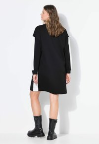 Vestido negro con paneles laterales blancos, de mangas largas y un corte relajado. Combinado con botas negras hasta la mitad de la pantorrilla que tienen grandes hebillas.
