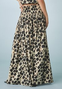 Jupe maxi en tissu beige avec un motif à pois noirs, dotée d'une taille froncée, d'un design fluide et de plis délicats.