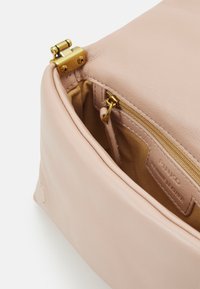 Borsa in pelle rosa chiaro con una chiusura dorata. L'interno presenta una tasca con cerniera e un'etichetta in pelle. Texture morbida e superficie liscia.