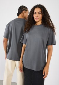 Grå bomulds T-shirt med korte ærmer og rund hals. Har en afslappet pasform og glat tekstur, vist på to modeller fra front og bag.
