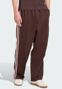 Brązowe, luźne spodnie dresowe z różowymi paskami po bokach. Wykonane z gładkiej tkaniny, z elastycznym pasem i bocznymi kieszeniami.