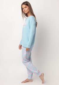 Sudadera azul claro con estampado rosa, combinada con pijamas de patrón en colores pasteles que presentan texto repetido. Tejido suave y corte relajado.