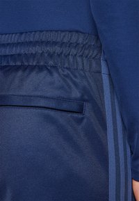 Marineblauwe sportbroek met een gestructureerde stof, elastische tailleband en subtiele zijkanten in een lichtere tint blauw, met een achterzak.
