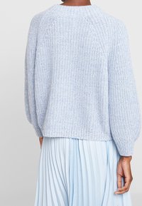 Hellblauer gestrickter Pullover mit geripptem Saum, puffigen Ärmeln und runder Ausschnitt. Strukturierter Garn sorgt für visuelles Interesse.