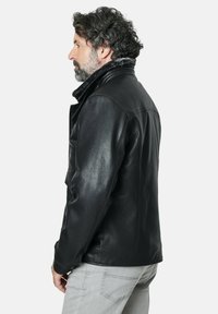 Chaqueta de cuero negra con un forro suave en el cuello, diseño ajustado, textura suave y bolsillo lateral. Modelo mostrado de lado.