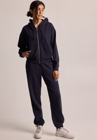 Navy blue hooded zip-up sweatshirt paired with matching joggers. Made of soft fabric, featuring pockets, relaxed fit, and elastic cuffs.