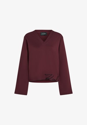 Burgundski dolg rokav s V-izrezom, ki ima črno vezeno besedilo ob robu. Mehka, struktura tkanina z sproščenim krojem.