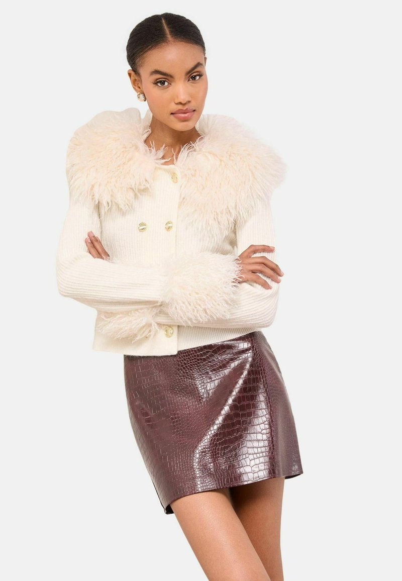 Krémový žebrovaný svetr s chlupatým límcem a manžetami, se zlatými knoflíkovými zapínáními, skombinovaný s lesklou sukní z bordeaux krokodýlí embosované kůže.