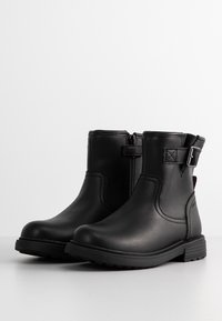 Paire de bottines noires avec fermetures éclair latérales et sangles réglables à boucle, dotées de talons carrés bas et de semelles texturées.