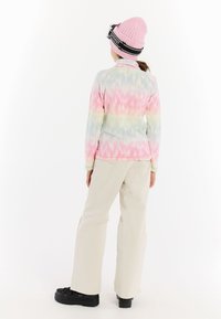 Barevná fleecová bunda s růžovým, modrým a zeleným tie-dye vzorem; spárovaná s béžovými kalhotami a černými platformovými botami. Na hlavě má růžovou pletenou čepici.