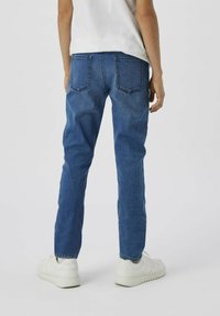 Pantalones vaqueros de mezclilla azul con corte recto, que cuentan con dos bolsillos traseros y un lavado medio. Llevados con zapatillas blancas, mostrados por la parte de atrás.