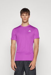 Camiseta deportiva morada hecha de tela suave, con un cuello redondo y mangas cortas, y un pequeño logo blanco en el pecho.