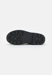 Semelle extérieure en caoutchouc noir avec un motif de traction texturé, comportant des rainures profondes et des crampons pour une adhérence, des bords lisses et une zone de talon renforcée.