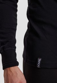 Svart langermet skjorte med en tettsittende design. Har ribbede mansjetter og et merke på den nedre siden som viser merkenavnet "DOVRE."