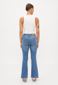 Valkoinen ilman hihnoja oleva pusero, jossa on aaltoilevat reunat, yhdistettynä vaaleansinisiin leveälahkeisiin farkkuihin, jotka esittelevät klassista denim-kangasta ja retro-tyyliä.