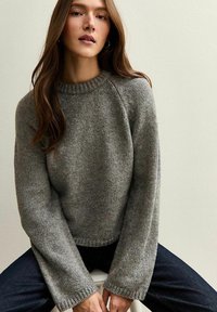 Grijze gebreide trui met een ribbelboord ronderole en brede mouwen, met een zachte textuur en een licht verkorte pasvorm.