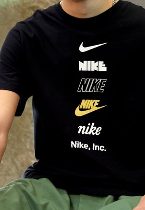 Schwarzes Baumwoll-T-Shirt mit mehreren Nike-Logos in verschiedenen Schriftarten und Farben, darunter Weiß, Schwarz und Gold, auf der Vorderseite.