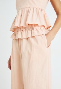 Conjunto de dos piezas color durazno que incluye un top corto con volantes y pantalones de pierna ancha con una cinturilla elástica y bolsillos laterales.