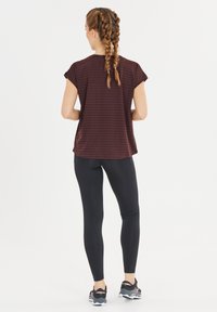 Bordeaux gestreepte top met korte mouwen gecombineerd met zwarte leggings. De top heeft een relaxte pasvorm, terwijl de leggings aansluitend en glad zijn.