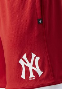 Shorts de sport rouges en tissu texturé, arborant un logo blanc NY bien visible et une petite étiquette noire 47 sur le côté.