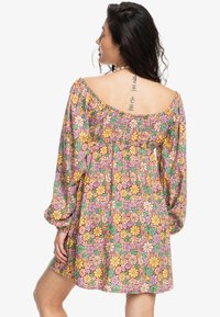 Vestido de estampado floral con mangas largas abullonadas, que presenta un escote redondeado y cintura elástica. Los colores incluyen rosa, amarillo, verde y púrpura.