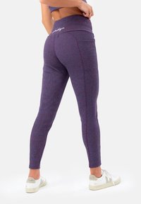 Leggings viola realizzati in tessuto texture, con una cintura larga, design aderente e cuciture decorative. Indossati con scarpe bianche.