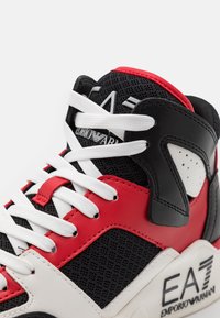 Czarno-czerwone sneakersy z siateczki i materiału skórzanego, grube białe sznurówki, wyściełany kołnierz oraz detal z logo po boku.