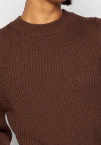 Brauner gerippter Pullover mit Rundhalsausschnitt, der aus einem strukturierten Stoff gefertigt ist und eine figurbetonte Silhouette hat. Hervorgehoben durch gleichmäßige vertikale Muster.