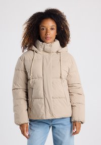 Giubbotto imbottito di un beige chiaro con colletto alto, cappuccio con cordoncino e design trapuntato. Presenta una chiusura frontale a pressione e tasche laterali.