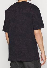 Černé texturované tričko s krátkým rukávem, kulatým výstřihem a volným střihem, s vybledlým vzhledem a hladkým materiálem.