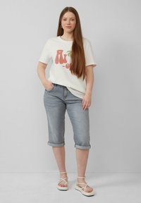 Crème t-shirt met kleurrijk tekstontwerp, in combinatie met opgerolde grijze denimshorts en witte bandjesandalen. Effen kleur, casual pasvorm.