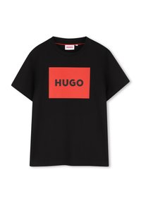 Svart bomulls-t-shirt med en röd rektangulär logotyp där "HUGO" är tryckt i svart. Rund halsringning och korta ärmar, standardpassform.