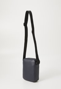 Navy synthetic material crossbody bag with a square shape, adjustable black strap, and smooth texture. Zipper closure along the top edge.