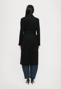 Zwarte mantel met een brede revers, lange mouwen en een rechte silhouet. Draag het over blauwe jeans en zwarte hoge schoenen. Glad textuur.