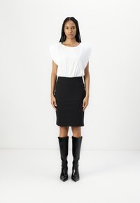 Blouse blanche à manches courtes avec taille froncée, associée à une jupe crayon noire ajustée et des bottes noires à talons droits montantes jusqu'aux genoux avec des bouts pointus.