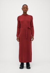 Κόκκινο πλεχτό μίντι φόρεμα με μακριά μανίκια, ριγέ μανσέτες και ζώνη στη μέση. Συνδυάζεται με μαύρες μποτάκια μέχρι τον αστράγαλο με αξεσουάρ πόρπης.