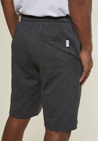 Dark gray athletic shorts made of soft fabric, featuring an elastic waistband, back pocket, and a small logo tag on the waistband.