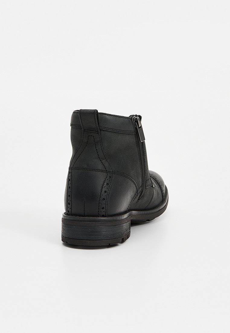 Bota de cuero negro hasta el tobillo con cremallera lateral, detalles brogue, acabado liso y tacón bajo apilado para mayor estabilidad.