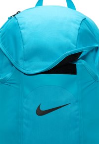 Turkis ryggsekk med klaff på toppen, teksturert stoff, og en svart Nike-logo på frontlommen. Synlig glidelås.