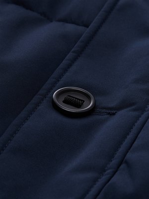 Tejido acolchado azul marino con una textura suave, que presenta un botón negro y un detalle de cordón en la superficie, destacando los patrones de acolchado.