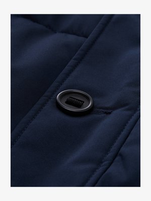 Tejido acolchado azul marino con una textura suave, que presenta un botón negro y un detalle de cordón en la superficie, destacando los patrones de acolchado.