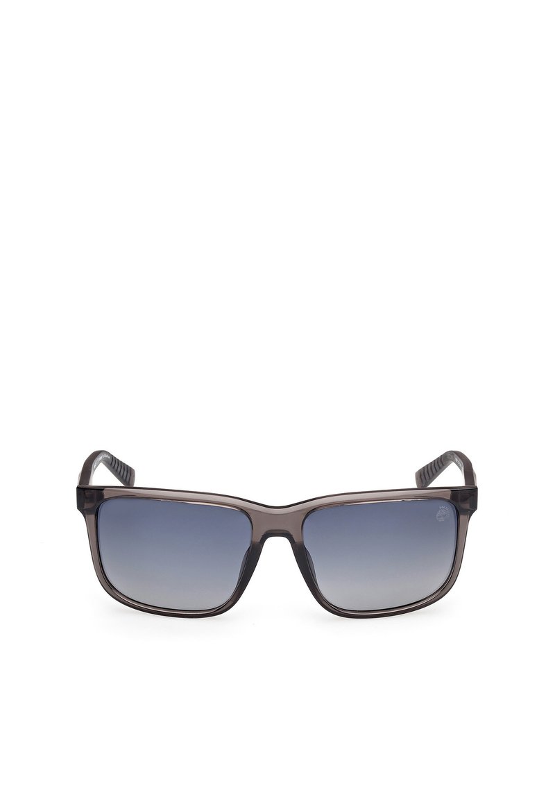 Gafas de sol con un marco de plástico transparente gris oscuro, lentes rectangulares que hacen la transición de un degradado oscuro a uno claro, y gomas texturizadas en las patillas.