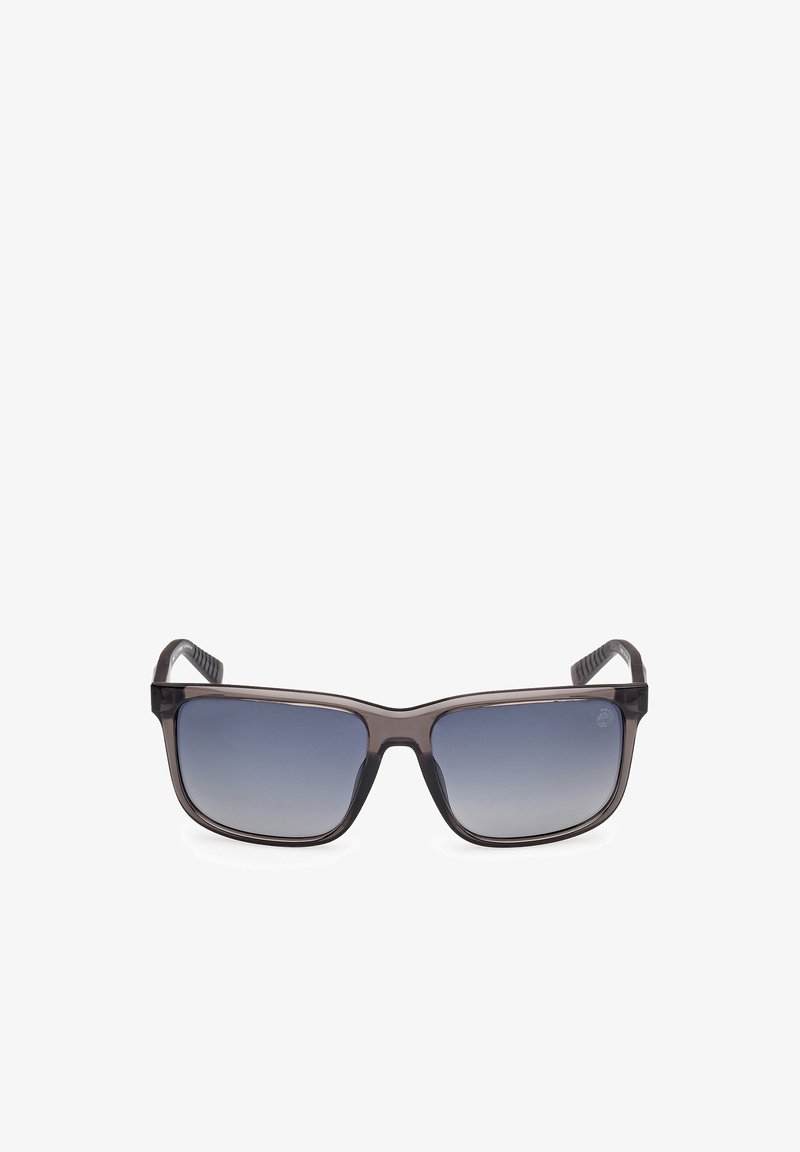 Gafas de sol con un marco de plástico transparente gris oscuro, lentes rectangulares que hacen la transición de un degradado oscuro a uno claro, y gomas texturizadas en las patillas.
