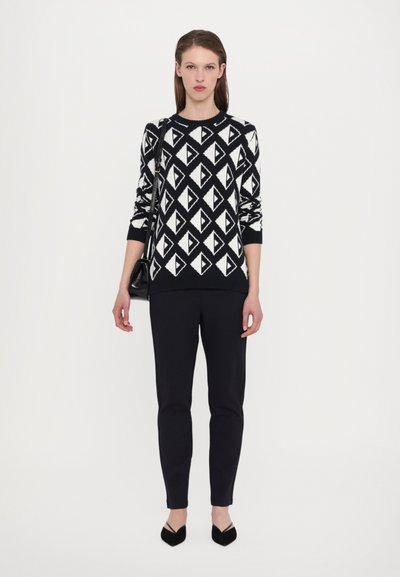 Pulover cu model alb și negru, cu forme triunghiulare, guler și manșete cu nervuri, asortat cu pantaloni negri ajustați și pantofi cu vârf ascuțit.