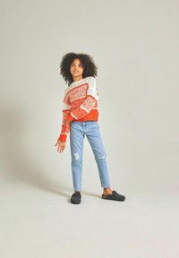 Maglione lavorato a maglia arancione e bianco con righe orizzontali, abbinato a jeans strappati blu chiaro e scarpe slip-on grigio scuro.