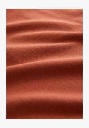 Rjavkasta tkanina z gladko teksturo, ki prikazuje mehke gube in gubice. Material se zdi lahek in diha.
