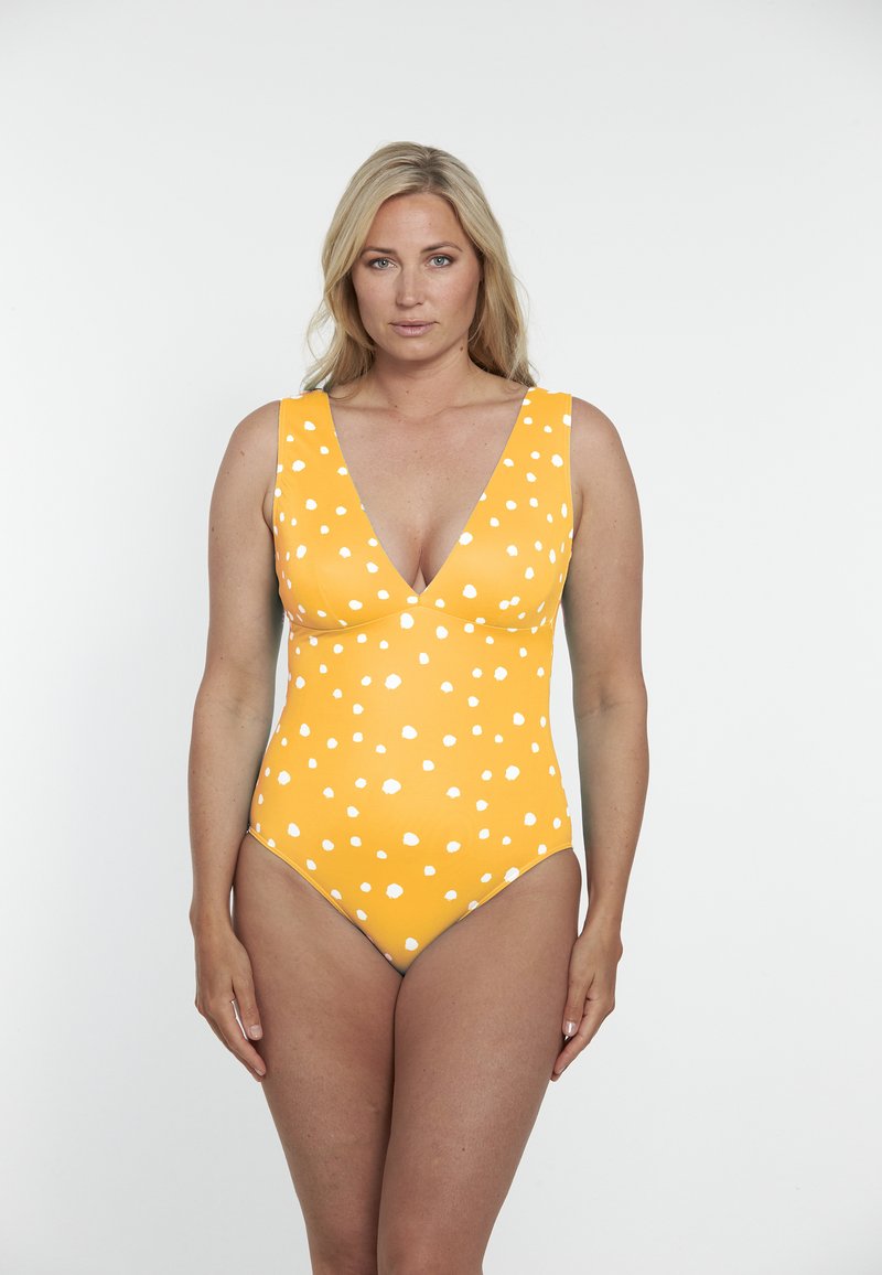 Maillot de bain une pièce jaune avec un décolleté en V profond, de larges bretelles et un motif de pois blancs sur un tissu lisse et extensible.