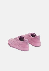 Pink athletic sneakers with a smooth finish, textured accents, and a chunky sole. Features lacing system and logo detail on the heel.