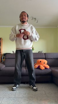 Sweater branco com detalhes em bordô e letra "B", jeans escuros, ténis preto e branco; polvo de pelúcia laranja num sofá cinzento.