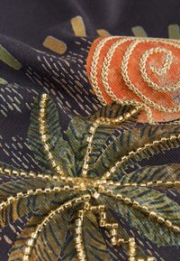 Tissu noir avec broderie en spirale orange, motifs de feuilles verts et ornements en perles dorées formant un motif floral.